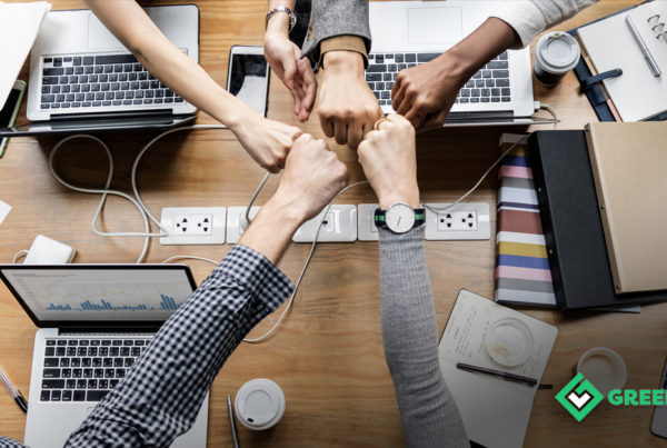 NewBossCommunications. A birds eye photo of a desk with 5 people fistbumping over laptops.